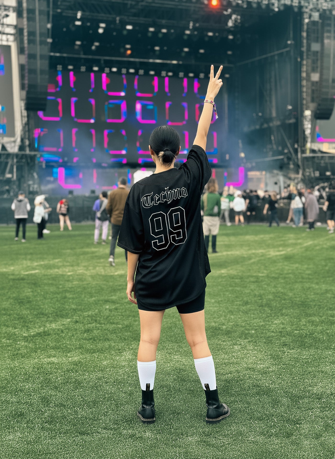 Person in a black sports jersey with 'Techno' and number '99' at an outdoor event with colorful stage lights.